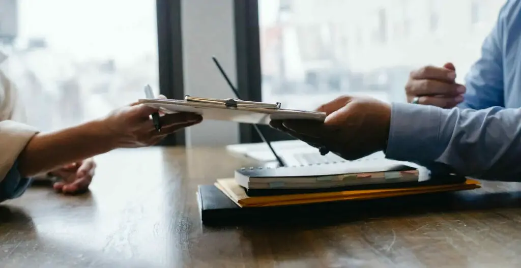 A man and a woman are sitting at a table an exchanging documents