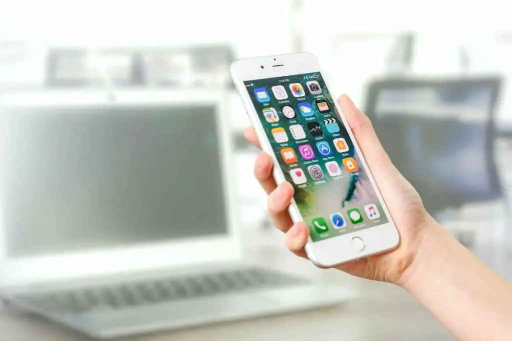 A woman is holding an iphone in front of a laptop