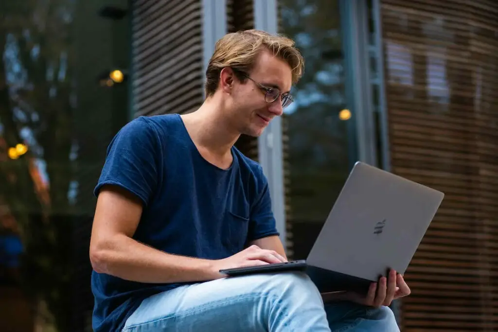 A young man sitting on a bench using a laptop