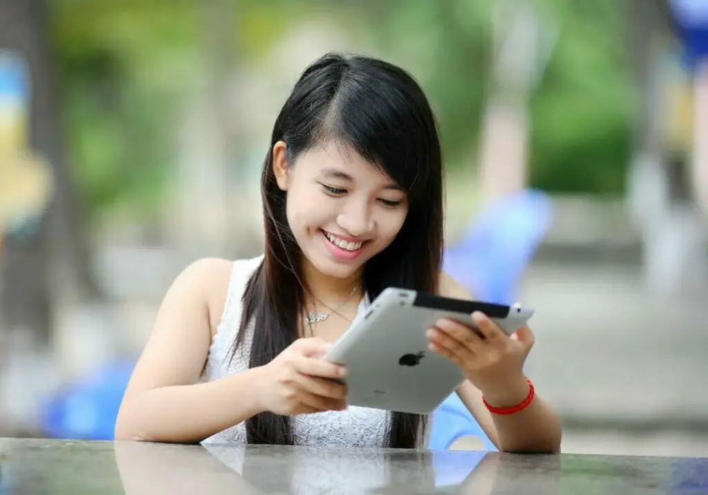 A young asian girl smiling while using a tablet computer