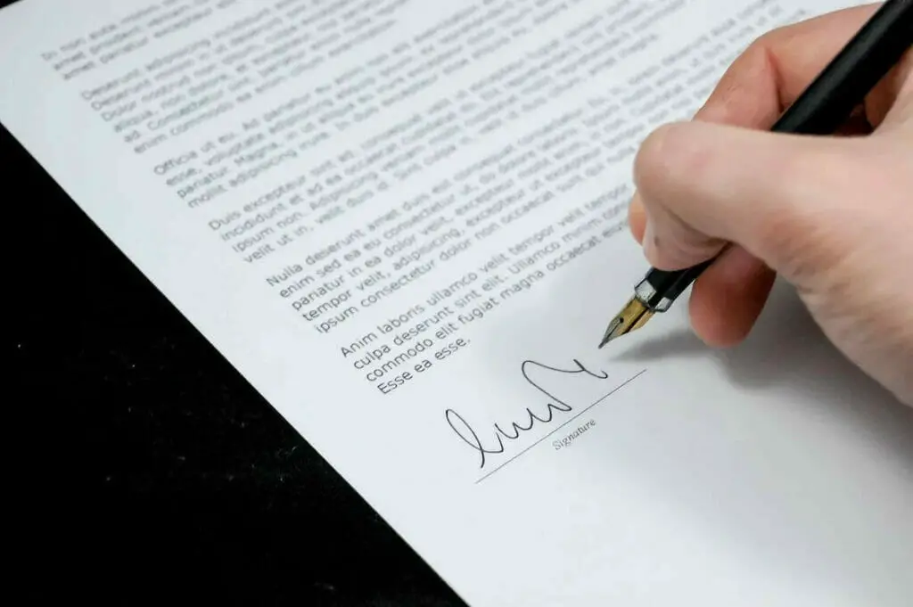 A person signing a document with a pen