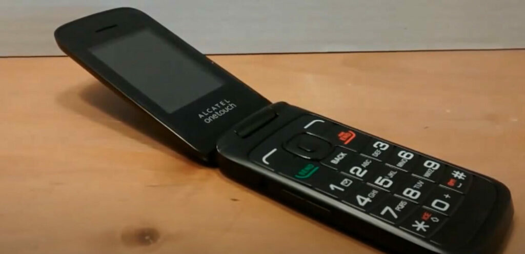 A black cell phone is sitting on top of a wooden table.