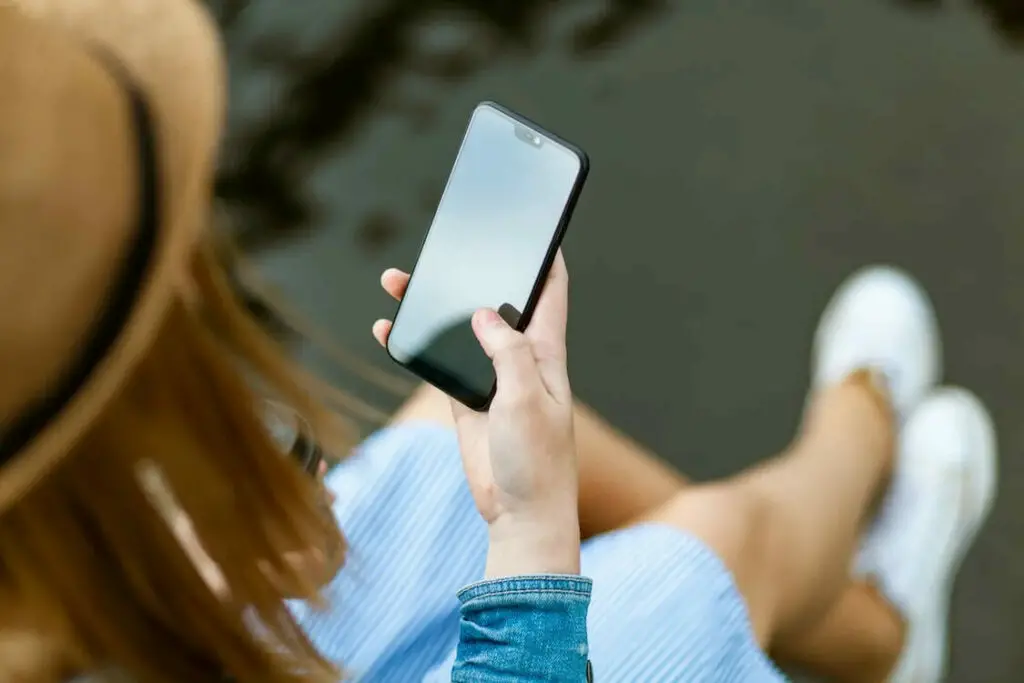 A woman is holding a smartphone while sitting on the ground.