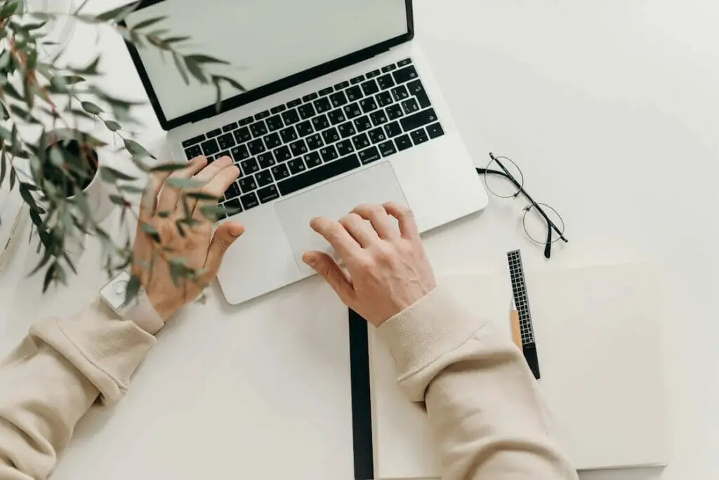 A topshot of a person working on his laptop in a cream white table