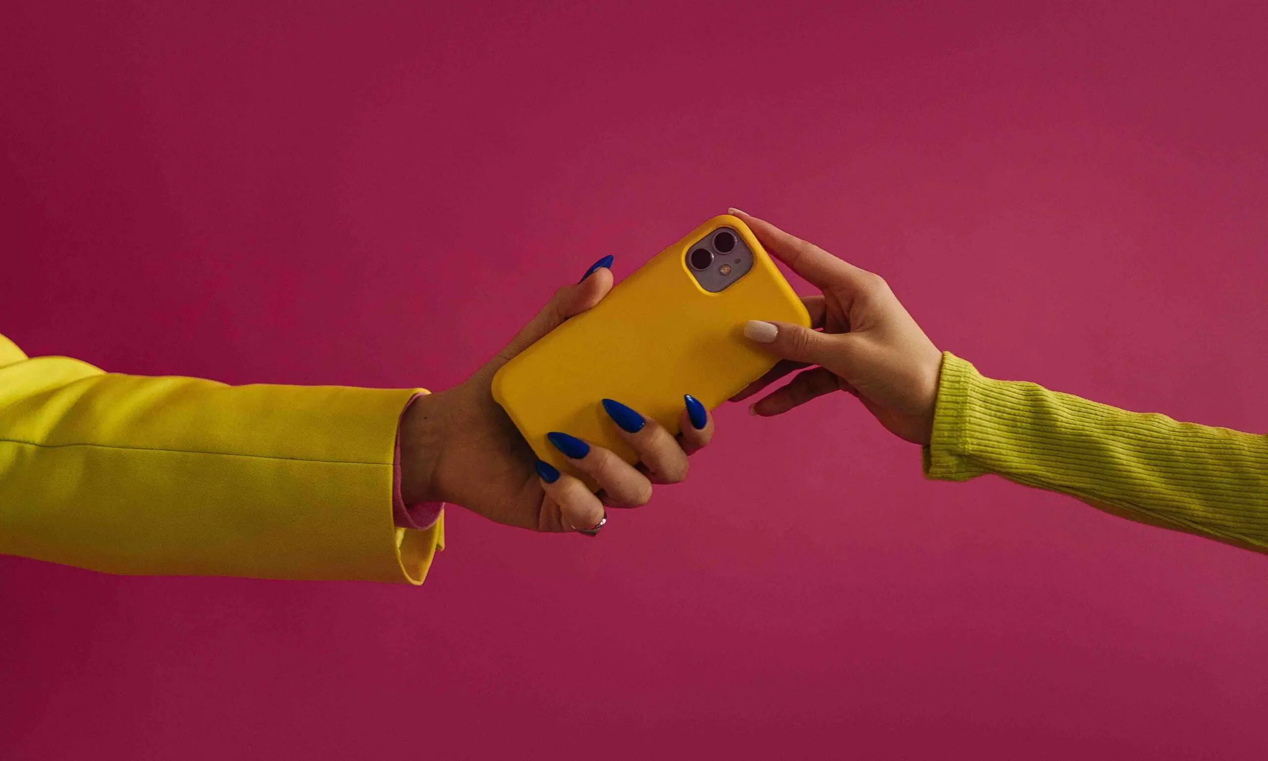 Two women in a pink background holding a phone with yellow casing